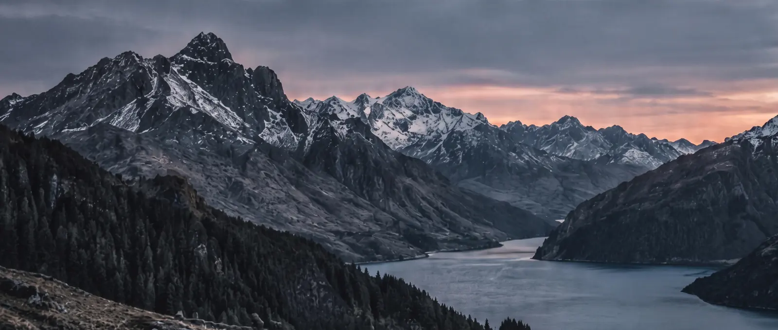 Snow-capped peaks above a winding lake near Queenstown at dusk