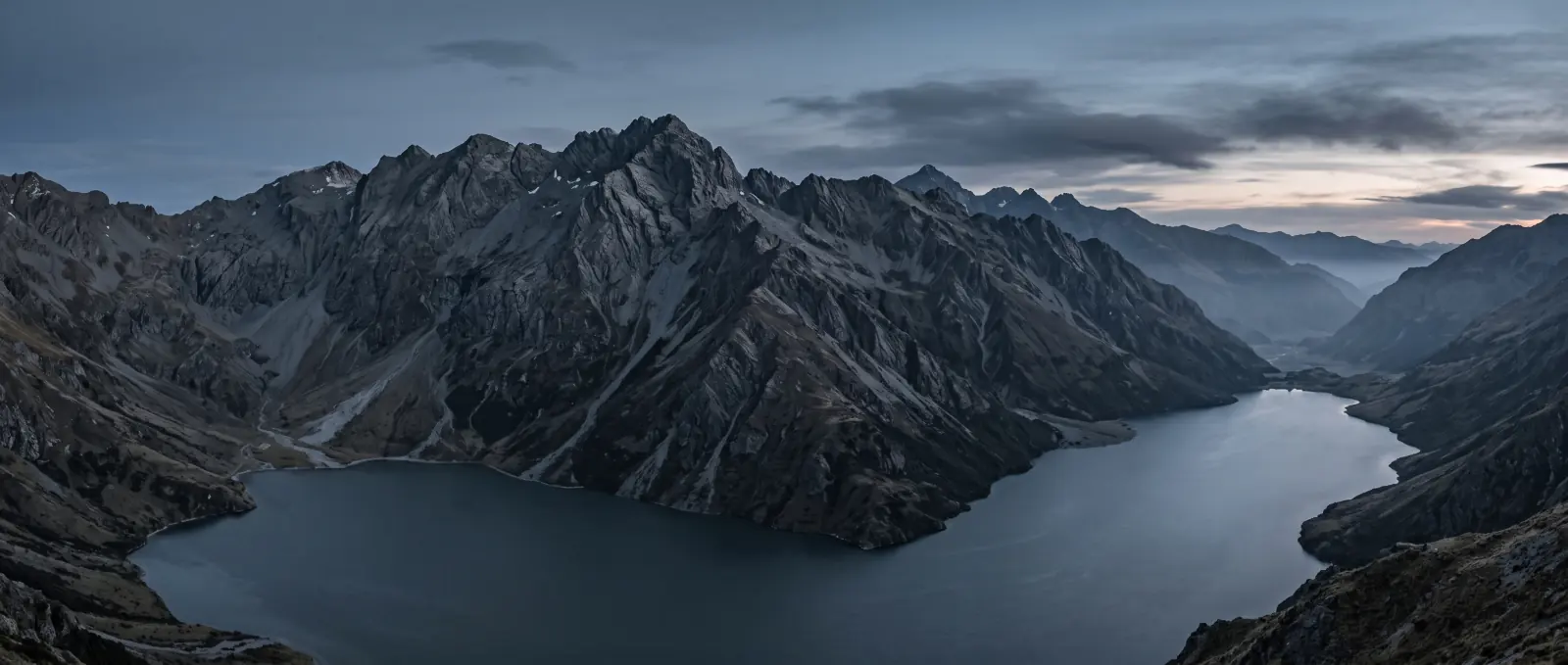 Snow-capped peaks above a winding lake near Queenstown at dusk